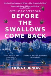 Link to the library catalogue entry for the book "Before the Swallows Come Back" by Fiona Curnow. The cover features a vibrant pink sky above a blue-toned forest and water landscape with flying swallows.
