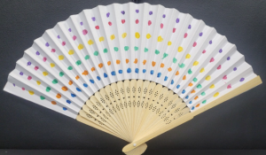 Photo of a decorated paper fan craft using dots and different colours. The fan is white.